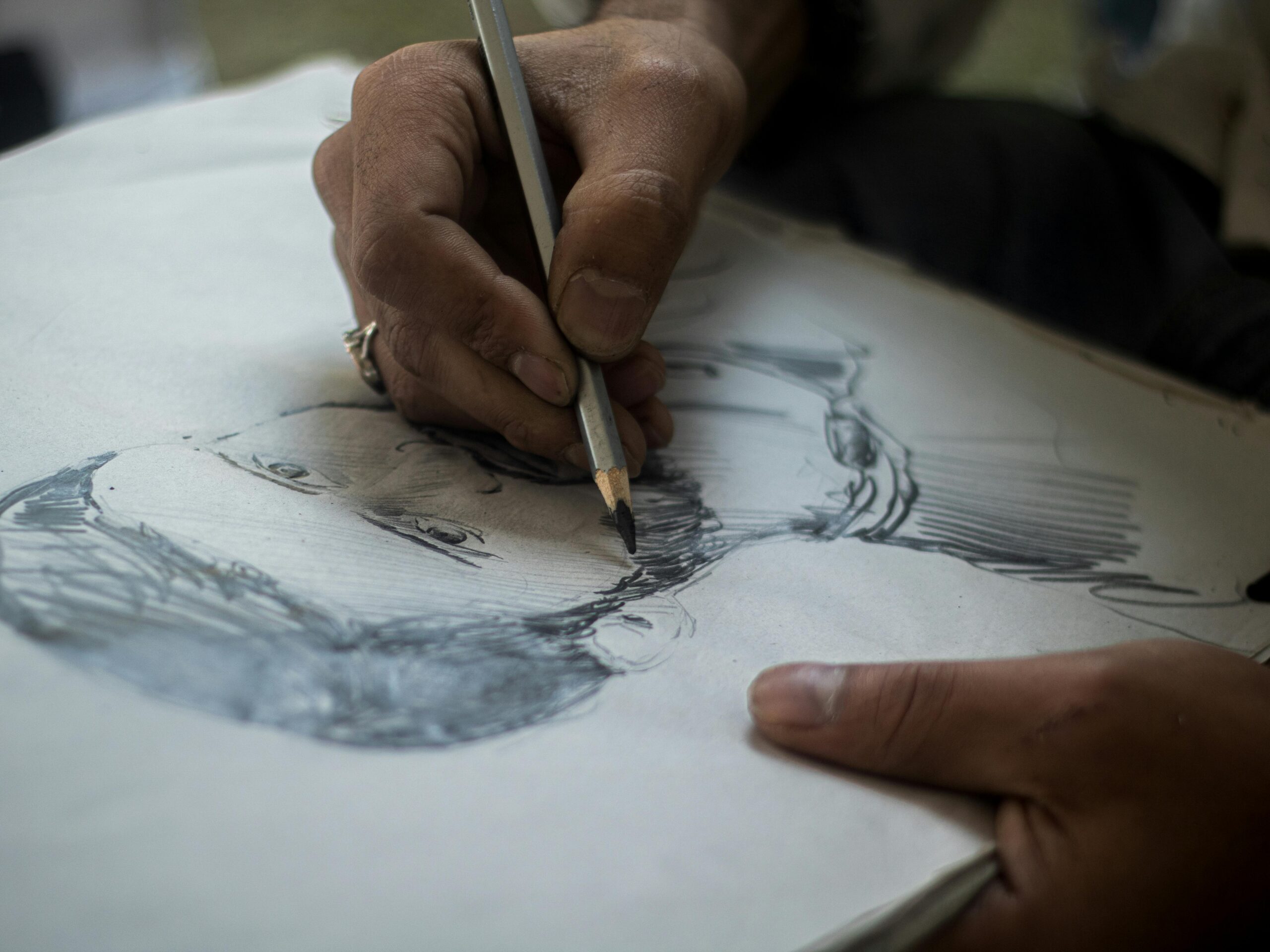 Detailed close-up of hands sketching a portrait with pencil on paper, highlighting artistic process.