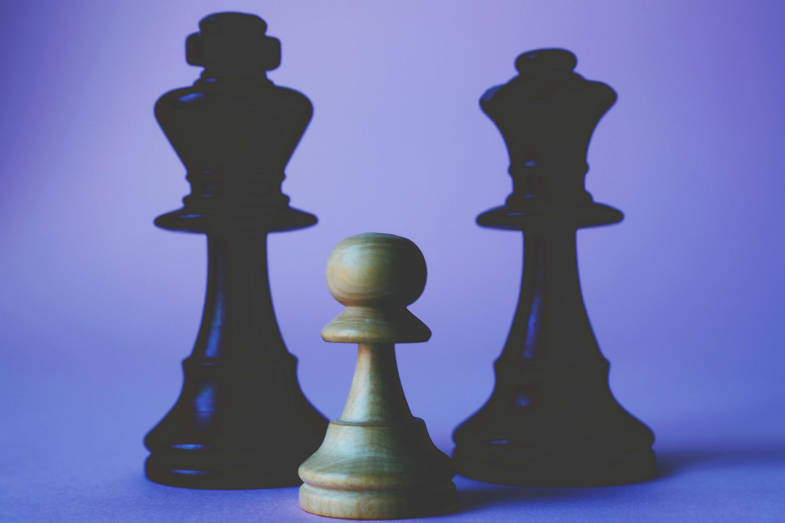 A close-up view of a pawn with queen and king chess pieces against a purple background.