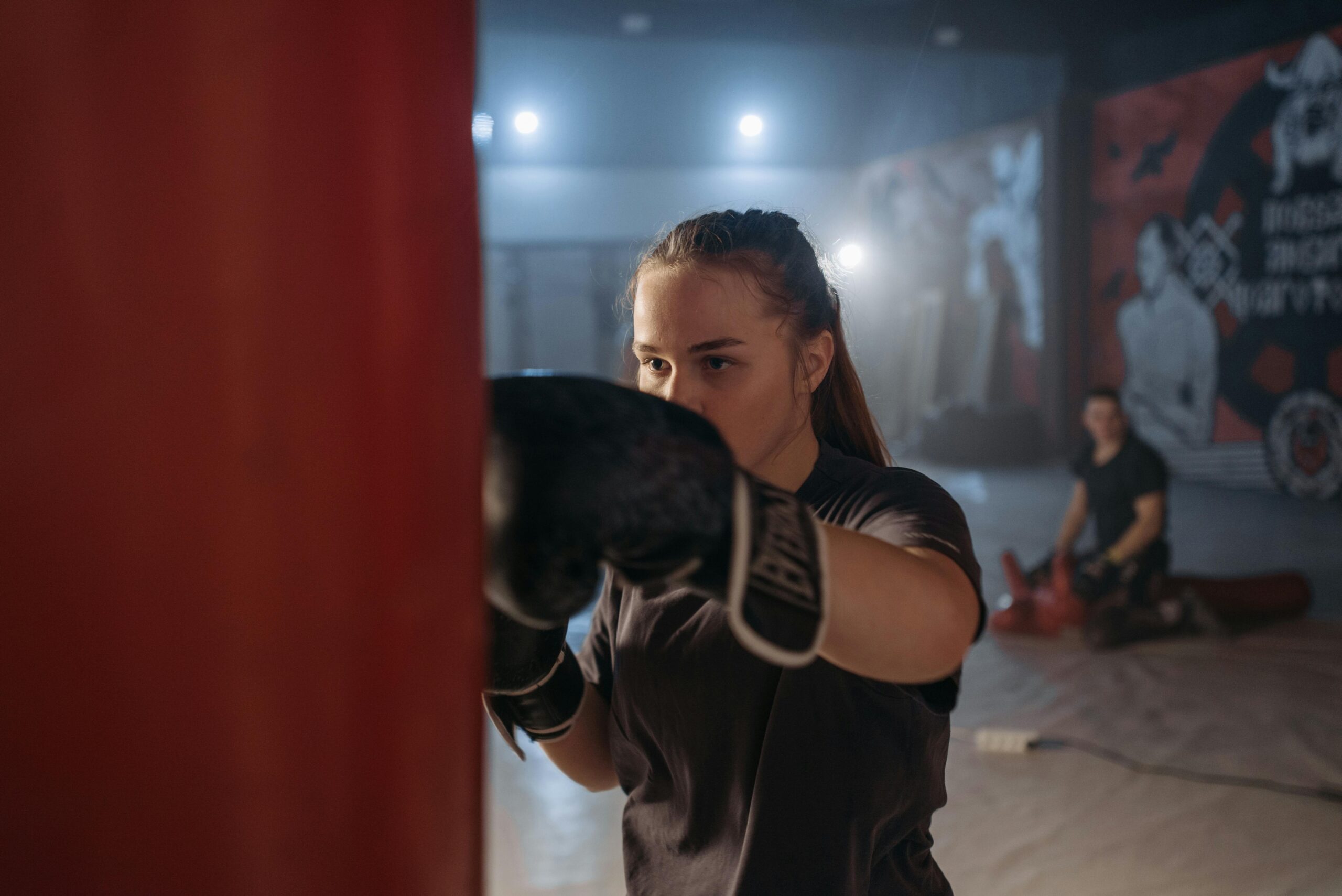 Focused young female boxer practicing her punches on a heavy bag in a gym setting.