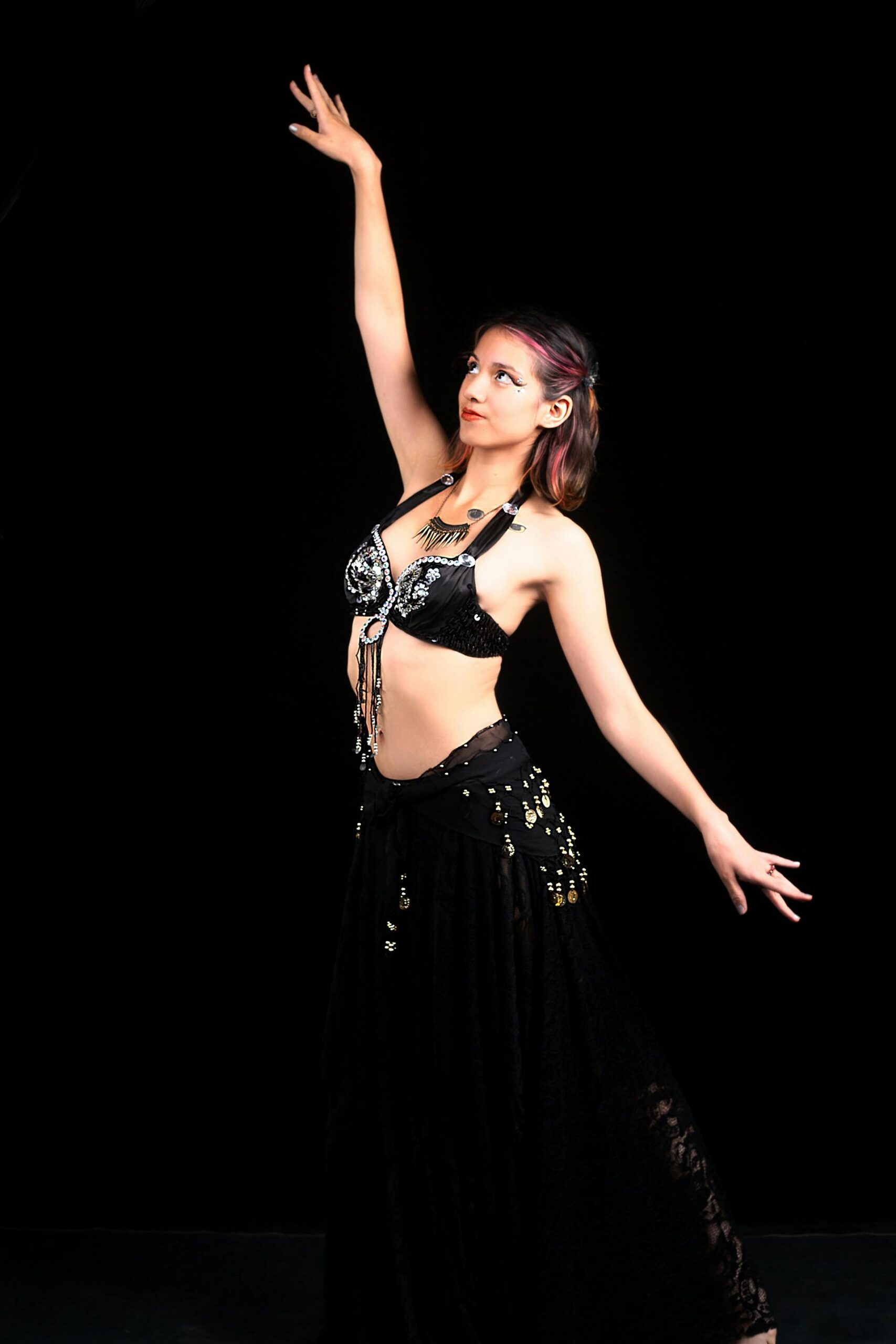 Young woman in belly dance costume striking a graceful pose in a studio setting.