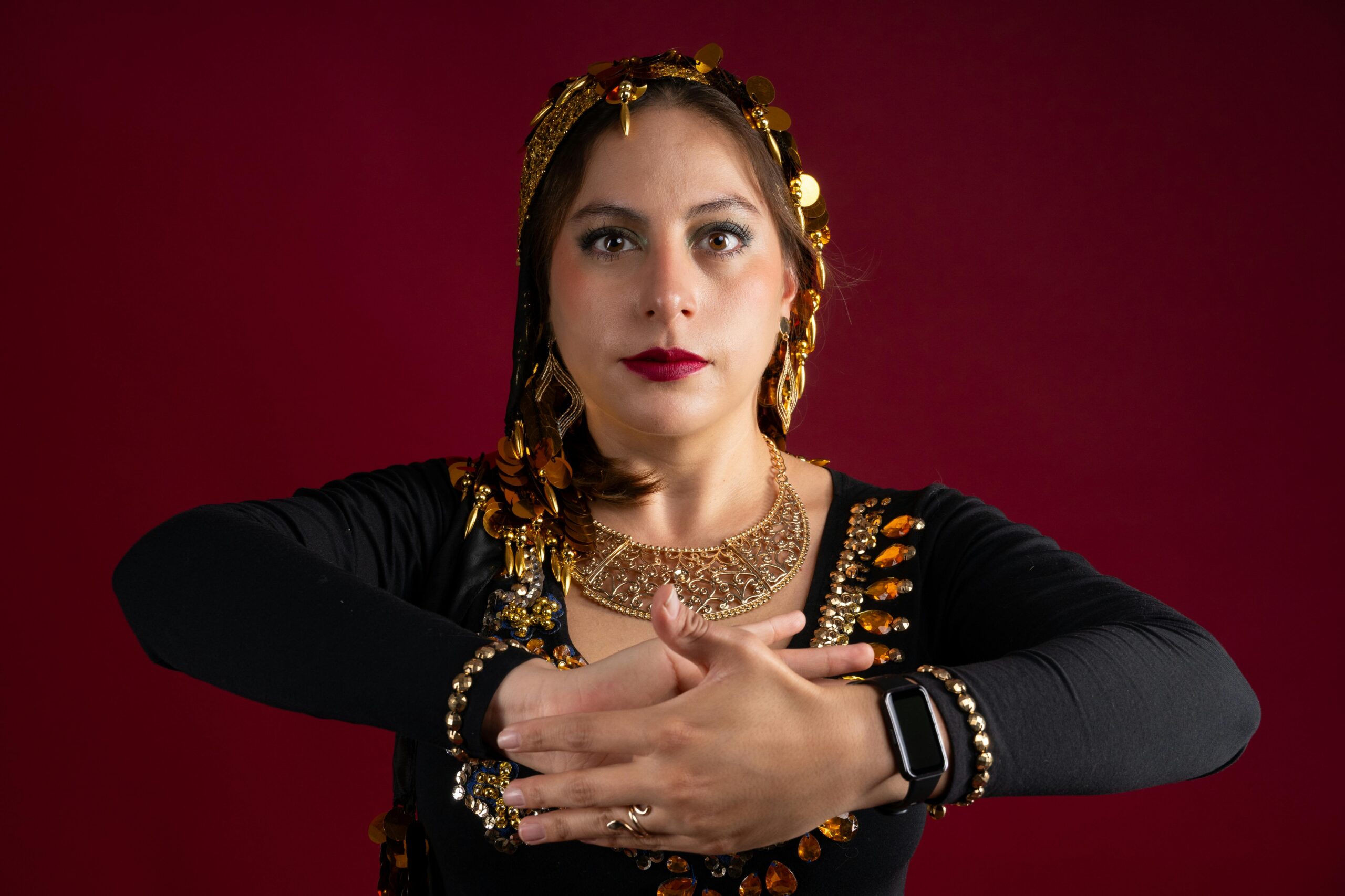 Portrait of a female dancer in traditional outfit with golden jewelry against a red backdrop.