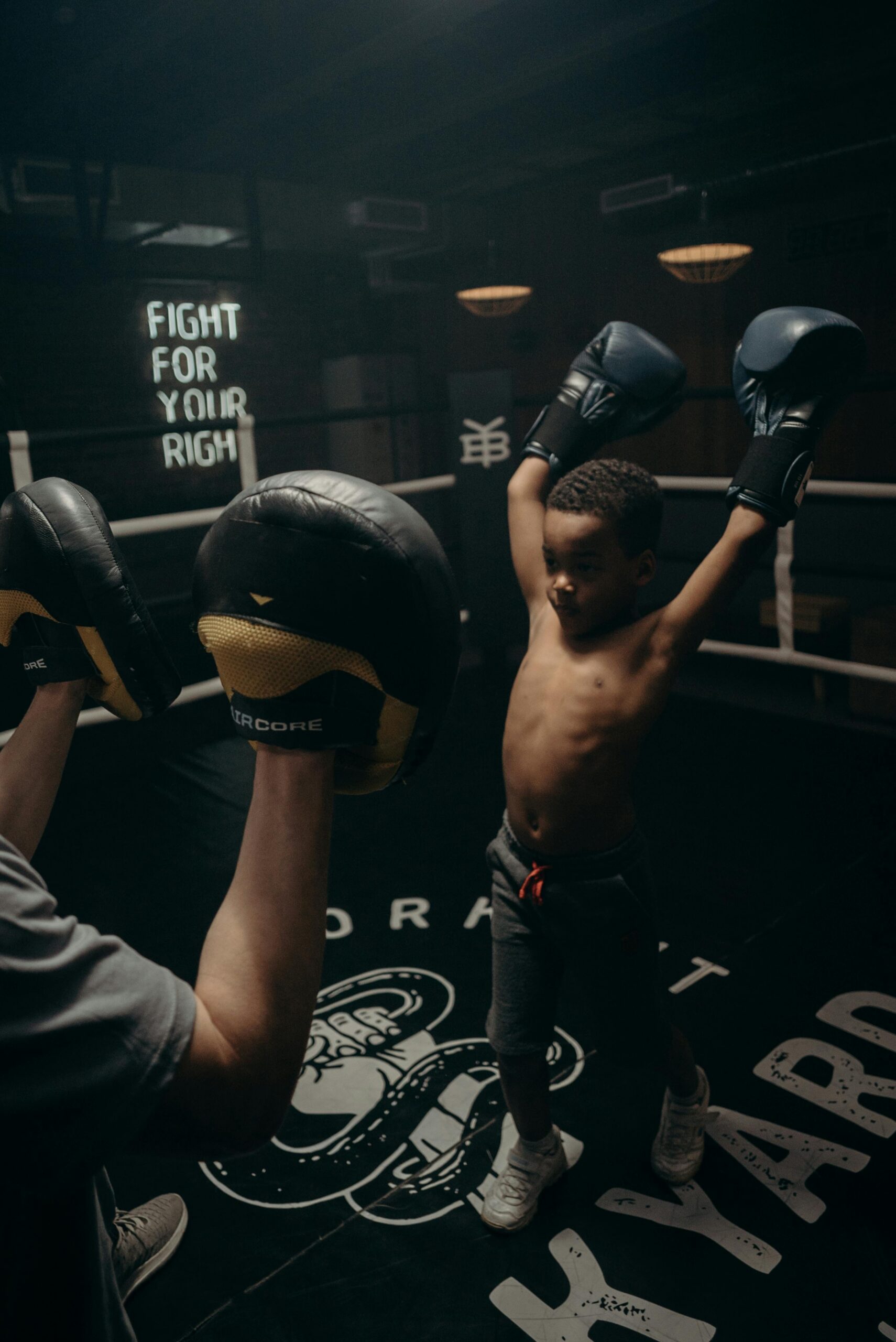A child boxer raises gloves in victory during sparring in a gym.