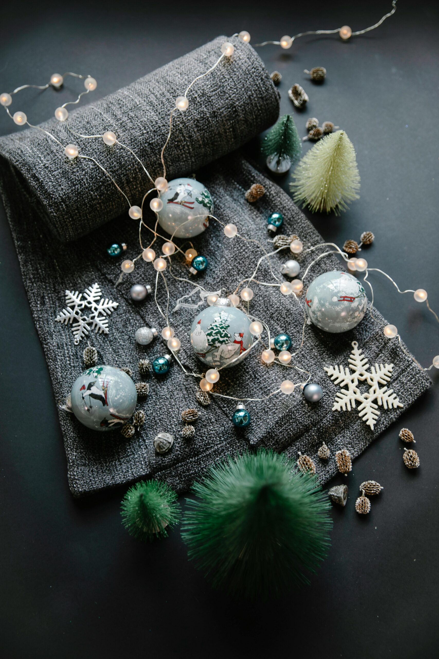 High angle of Christmas painted balls on textile near various decorations with small fake spruces and wreath on black surface