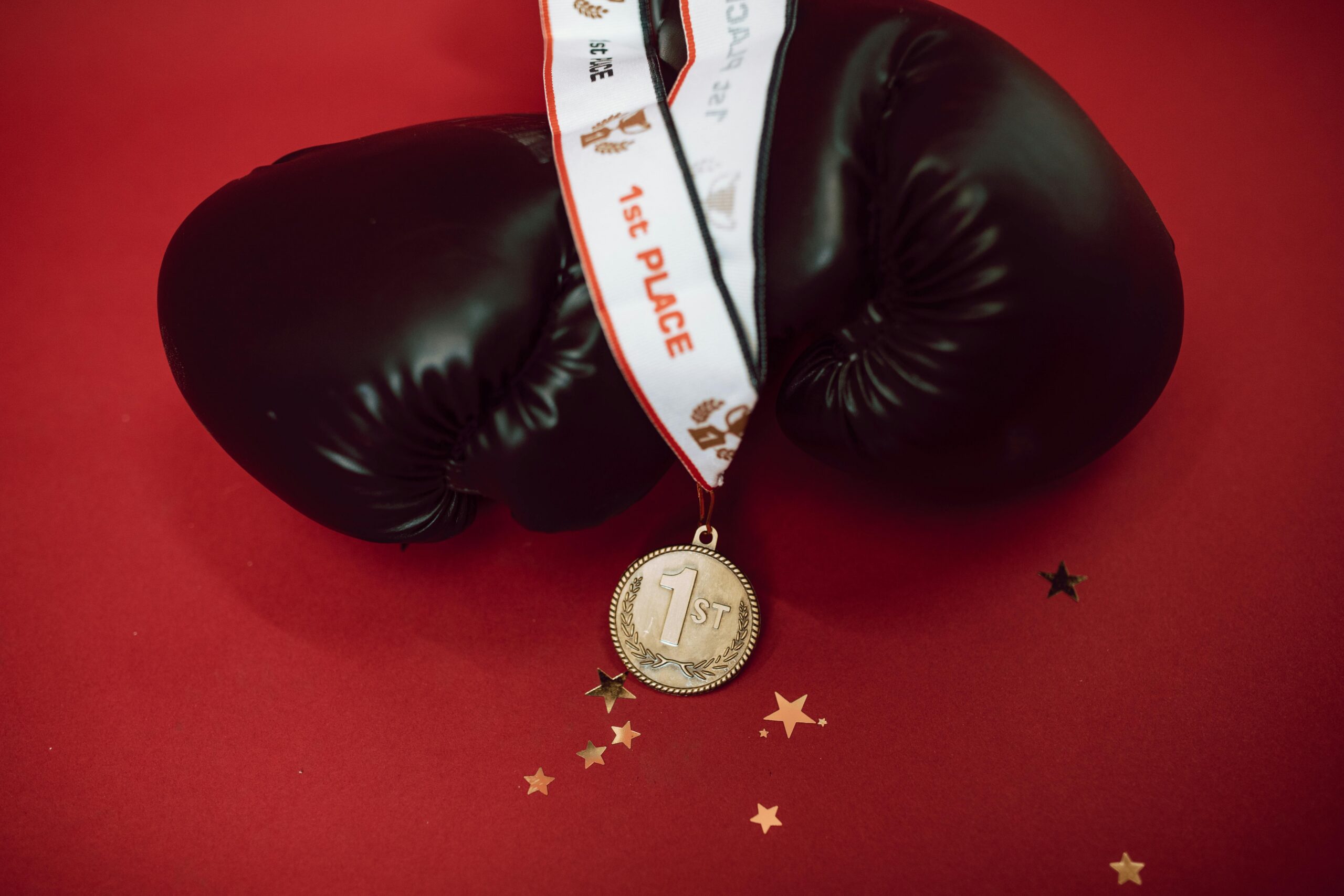 Black boxing gloves with a gold medal on a red background, symbolizing victory and success.